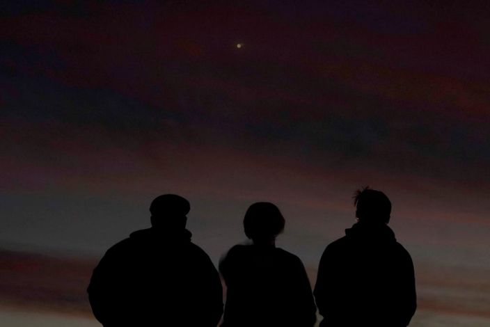 Le persone sono all'ombra di fronte al cielo al tramonto mentre guardano l'allineamento di Saturno e Giove, lunedì 21 dicembre 2020, a Edgerton, Cannes.